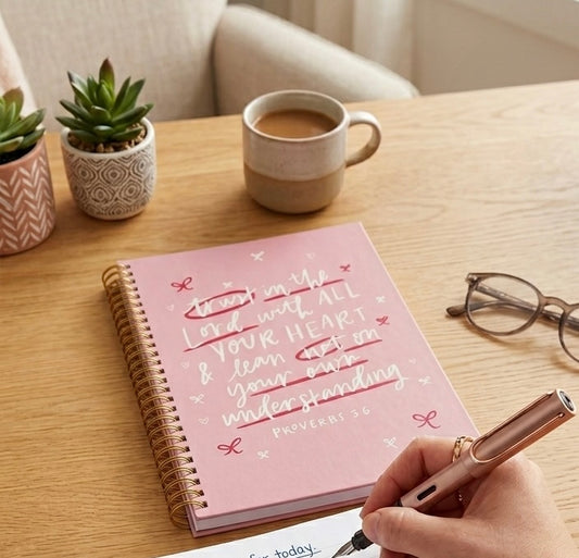 Woman writing in an Angelic Proverbs 3:6 journal at a wooden desk with a coffee mug, representing a peaceful morning devotional routine.