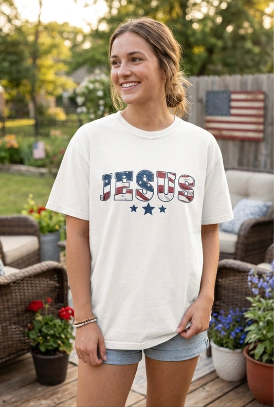 A woman wearing a patriotic "JESUS" graphic t-shirt with an American flag design in a backyard setting