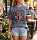 A woman wearing a blue Christian t-shirt with a butterfly, cross, and the scripture quote Created With A Purpose, Ephesians 2:10.