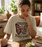 A lifestyle shot of a woman in a light-colored Christian t-shirt, reading a Bible with houseplants, featuring the Created With A Purpose butterfly design.