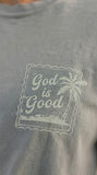 Close-up detail of a sage green Christian t-shirt featuring a minimalist "God is Good" palm tree stamp design on the chest.