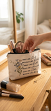 "A close-up mockup of a beige canvas cosmetic pouch resting on a wooden vanity. The pouch features a floral design and the inspirational text: 'Wait like Sarah, Protect like Rahab, Trust like Ruth, Pray like Hannah, Lead like Esther, Rejoice like Mary.'"