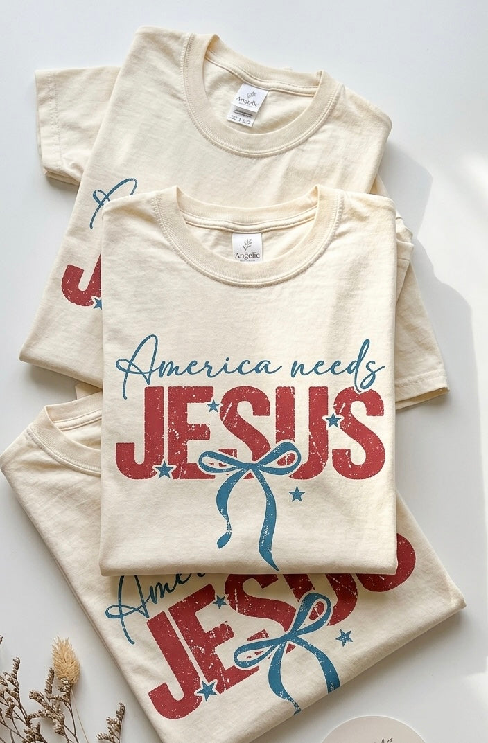 A flat-lay or folded view of multiple America Needs Jesus shirts, highlighting the heavy-cotton graphic tee design and aesthetic.
