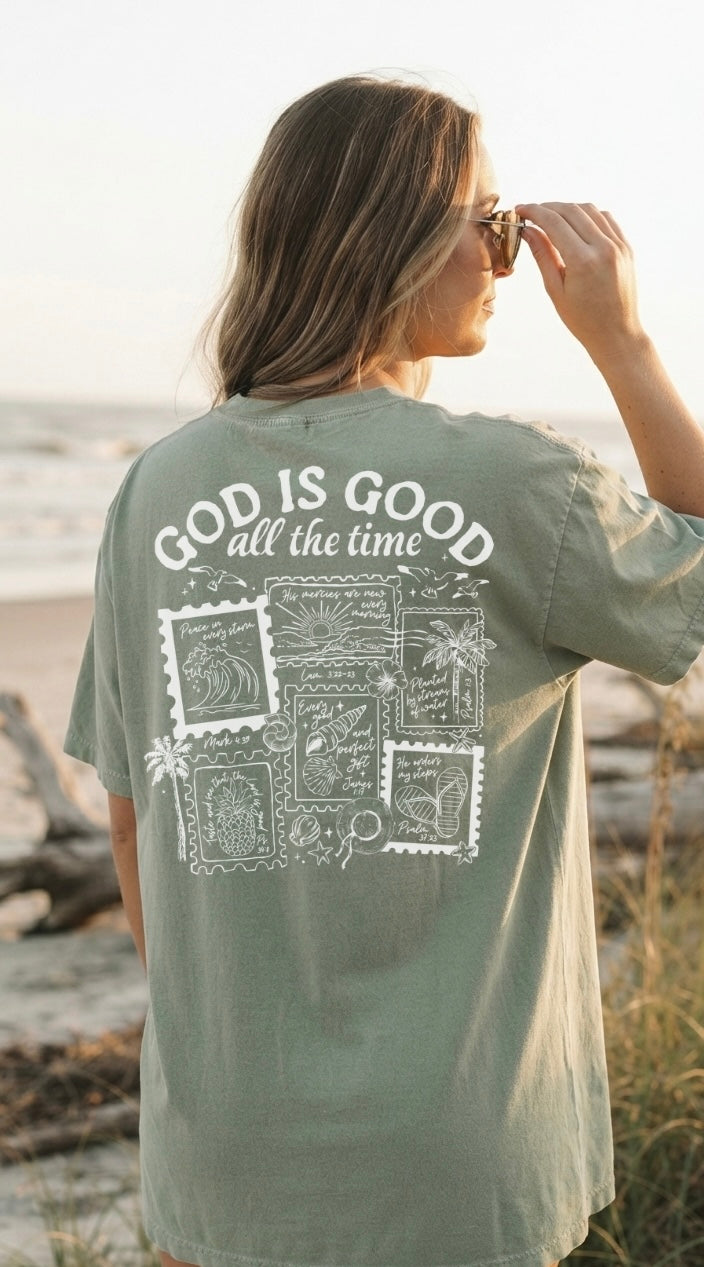 Back view of a woman wearing a faith-based inspirational clothing tee featuring a detailed "God is Good all the time" coastal graphic