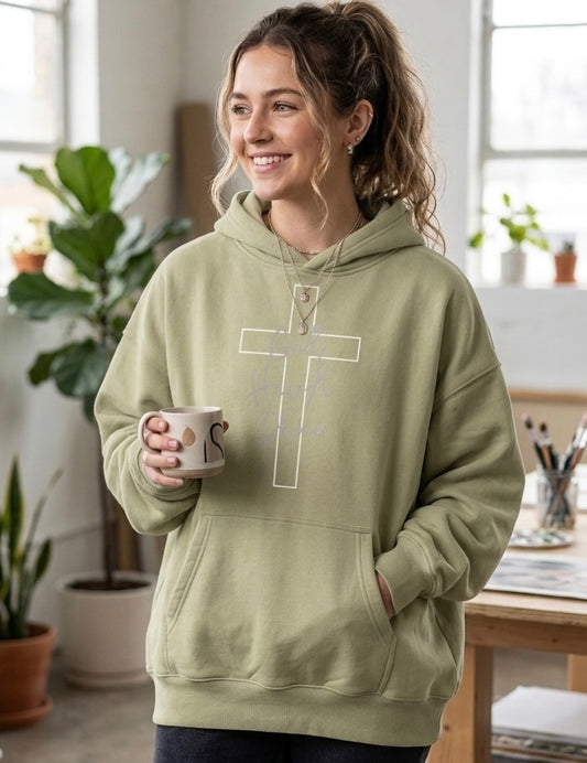 A woman wearing a Christian baggy, light green hoodie with a cross design on the front, holding a coffee mug in an art studio