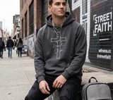 A man wearing a dark grey "God Has A Plan" Christian hoodie in an urban streetwear setting with a brick wall background