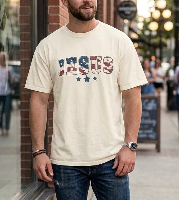 trendy man wearing an ivory patriotic "JESUS" graphic t-shirt and blue jeans, styled for urban Christian street wear.