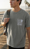 Man wearing a sage green Christian streetwear t-shirt with a "God is Good" palm tree stamp design on the chest