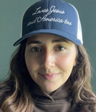 Woman wearing a navy blue Christian faith-based trucker hat with Loves Jesus and America too embroidery.