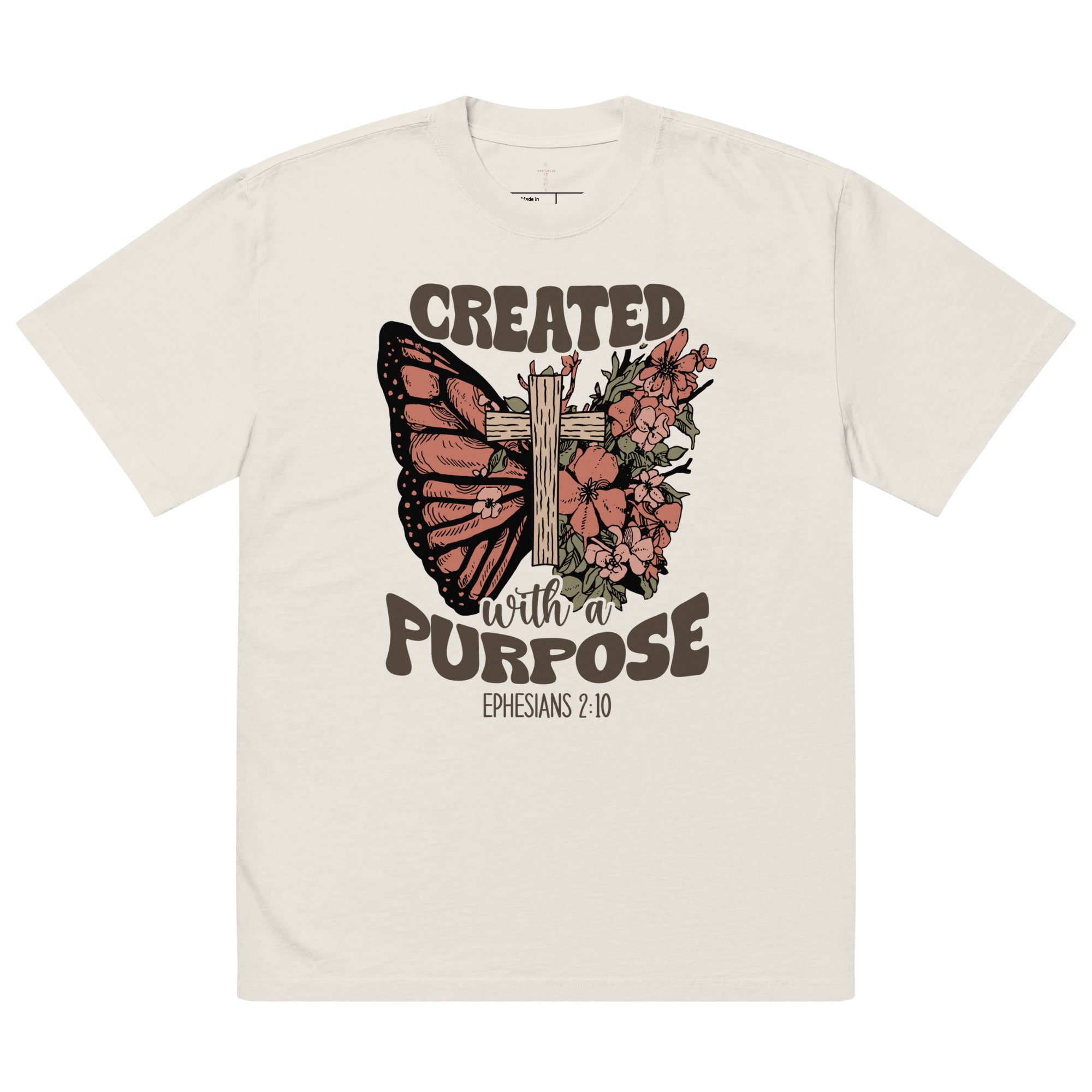 An isolated product view of a cream oversized faded t-shirt with a Christian graphic showing a butterfly, cross, and the quote Created With A Purpose