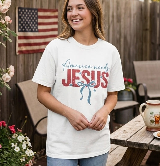 A lifestyle photo of a woman in an America Needs Jesus t-shirt standing in front of an American flag, casual faith-based fashion.