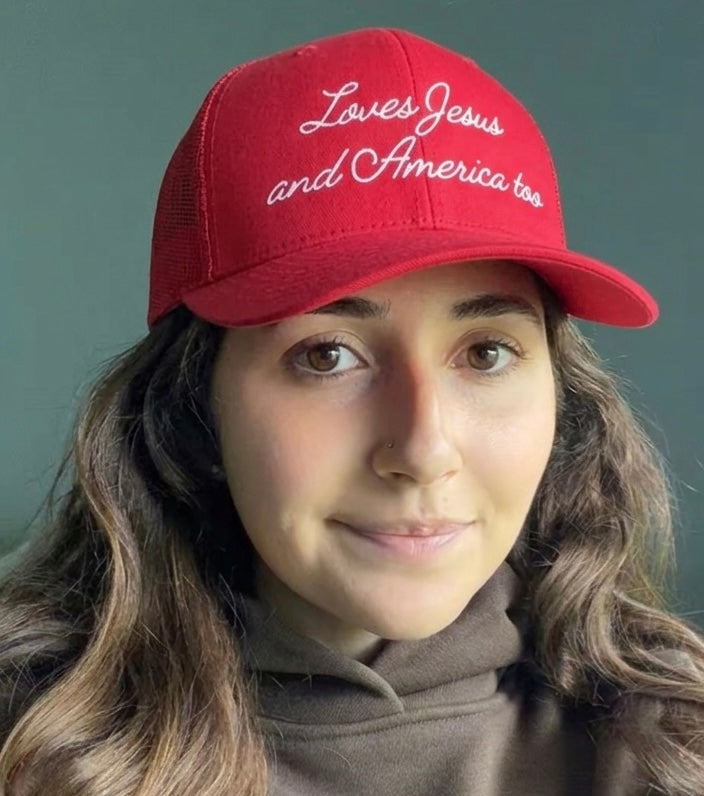 Woman wearing a red Christian trucker hat embroidered with the phrase Loves Jesus and America too