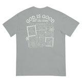 Flat lay back view of a sage green faith-based t-shirt featuring a "God is Good all the time" stamp-style inspirational graphic.