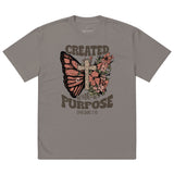 An isolated product view of a grey-brown vintage-style Christian t-shirt with a graphic of a butterfly, cross, and the scripture Created With A Purpose.